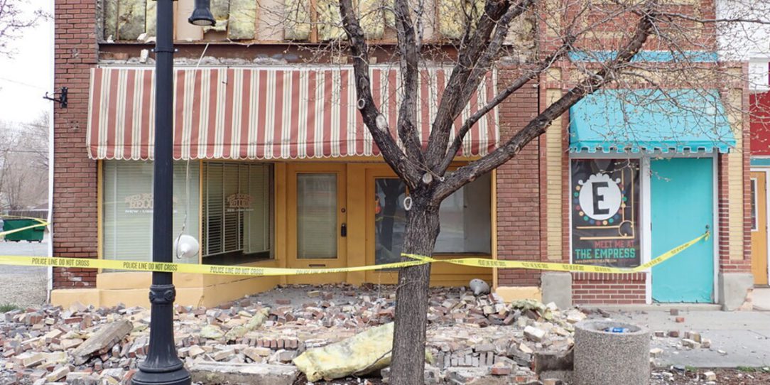 Storefront roped off with caution tape and bricks broken on the ground.
